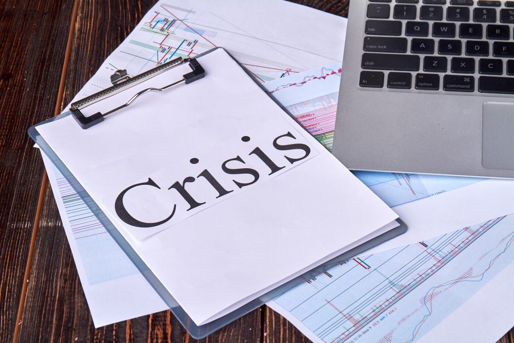 Clipboard with crisis word and laptop on the desk.